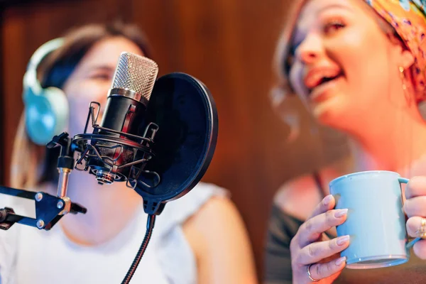 two young women behind the mic while streaming radio podcast - selective focus on microphone