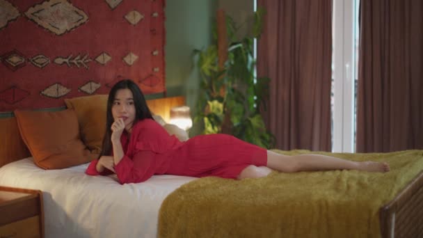 Kırmızı Yazlık Elbiseli Güzel Asyalı Kadın Pencereden Bakmak Için Yataktan — Stok video