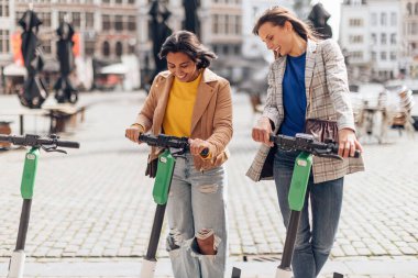 Şehir merkezinde e-scooter kullanan iki şık bayan arkadaş.