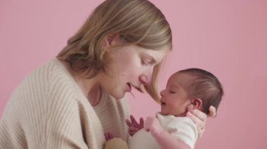 Anne yeni doğmuş çocuğuna sarılıyor ve ona yapışıyor. Anne ve bebek pembe arka planda birlikte.