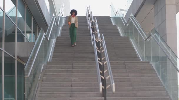 trendige Dame, die eine Außentreppe des Gebäudes hinuntergeht, in dem sie arbeitet - multi-ethnische und elegante Angestellte