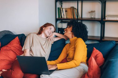 two young comfortable girls at home on couch with laptop