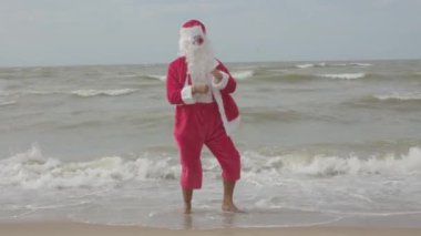 Mutlu noel babalar tatilleri. Deniz kıyısında dans ediyorlar. Noel seyahati, kış tatili.
