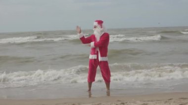 Mutlu noel babalar tatilleri. Deniz kıyısında dans ediyorlar. Noel seyahati, kış tatili.