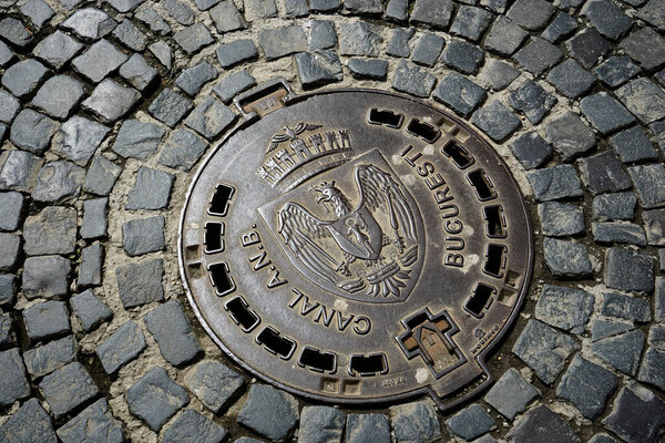 Bucharest, Romania - April 12, 2022: A canal cover with the emblem of Bucharest on a street paved with cobblestone in the old center. This image is for editorial use only.