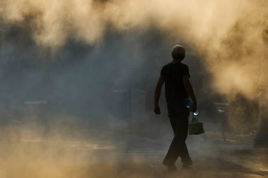 Bükreş, Romanya - 26 Temmuz 2022: Su şişesi taşıyan bir adam sıcak bir günde fıskiyenin ince bir spreyinde yürür. Bu görüntü sadece editoryal kullanım içindir.