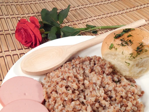 Porridge di grano saraceno, salsiccia, cucchiaio di legno e rosa — Foto Stock