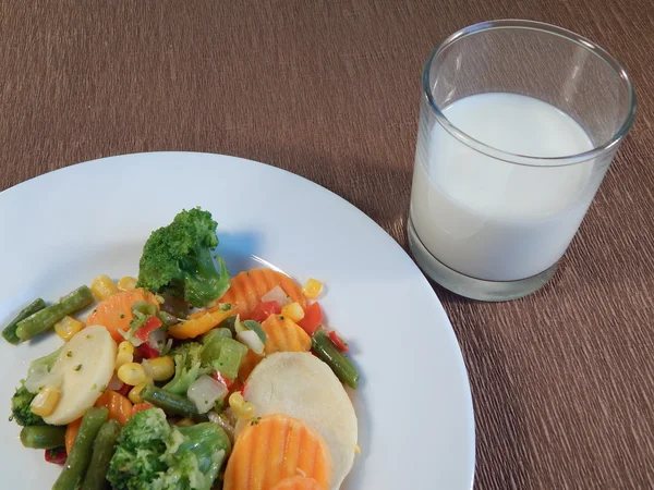 Gebratenes Gemüse auf dem Teller, brauner Hintergrund und ein Glas Milch — Stockfoto