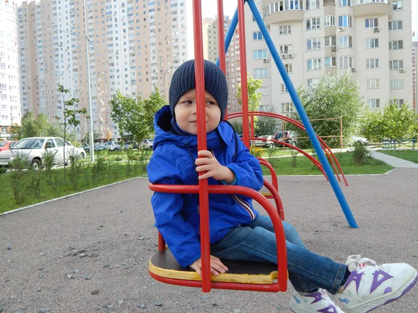 Un niño en un columpio en la ciudad — Foto de Stock