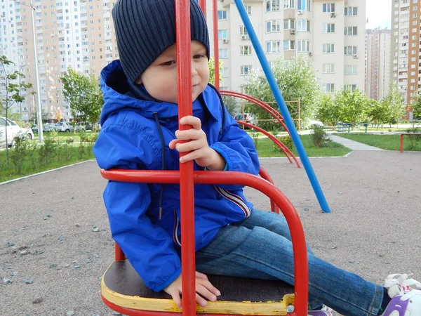 Un niño en un columpio en la ciudad — Foto de Stock