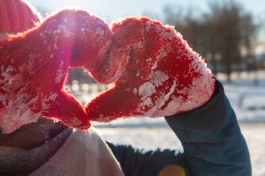 Red mittens in the form of a heart on white snow in winter