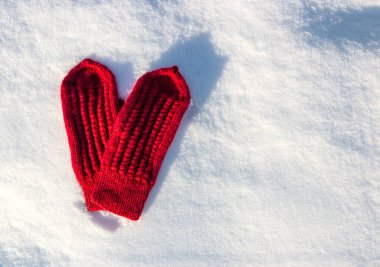 Red mittens in the form of a heart on white snow in winter