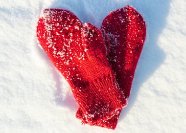 Red mittens in the form of a heart on white snow in winter