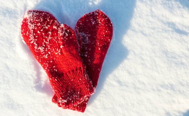 Red mittens in the form of a heart on white snow in winter