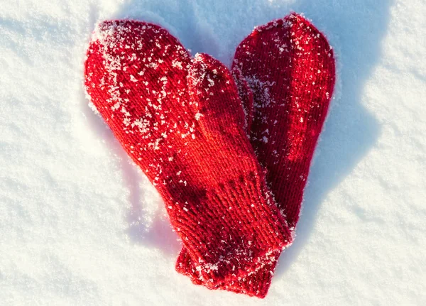 Red mittens in the form of a heart on white snow in winter