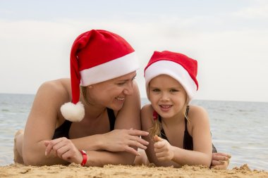 Kız annesiyle kumsalda Noel Baba şapkası