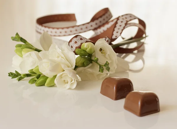 Sprig of freesia flower and chocolates — Stock Photo, Image