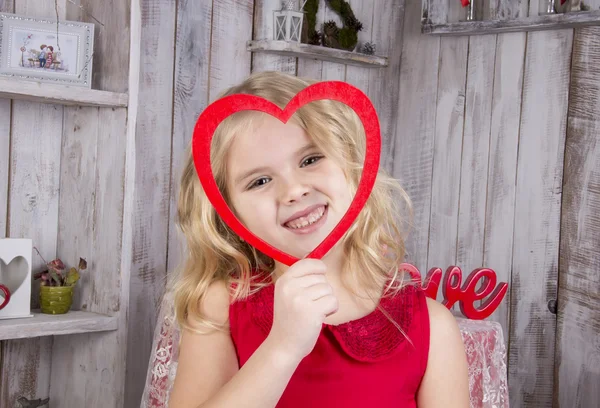 Dziewczyna wygląda i uśmiecha się przez klatkę w formie serca — Zdjęcie stockowe