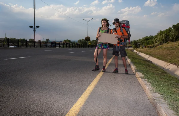 Dos amantes haciendo autostop, de pie con un cartel en blanco — Foto de Stock