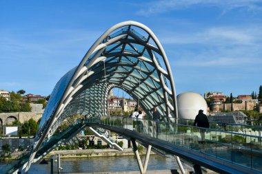 Tiflis, Gürcistan - 24 Ekim 2021: Barış Köprüsü, Gürcistan 'ın başkentinde bulunan Kura Nehri üzerindeki yaya köprüsü. Çelik ve cam yapımı. Köprüde yürüyen insanlar