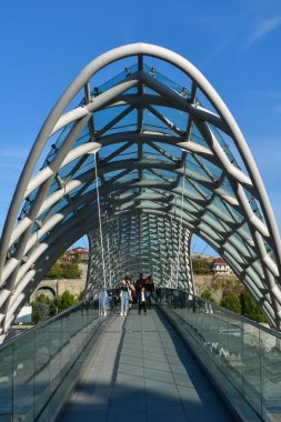 Tiflis, Gürcistan - 24 Ekim 2021: Barış Köprüsü, Gürcistan 'ın başkentinde bulunan Kura Nehri üzerindeki yaya köprüsü. Çelik ve cam yapımı. Köprüde yürüyen insanlar