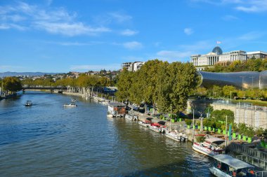 Tiflis, Gürcistan - 24 Ekim 2021: Gürcistan başkentinin Kura nehri, Cumhurbaşkanlığı Sarayı, Tiflis Müzik Tiyatrosu ve Konser Salonu ve Rike Park ile panoraması. Mavi gökyüzü, güneşli gün