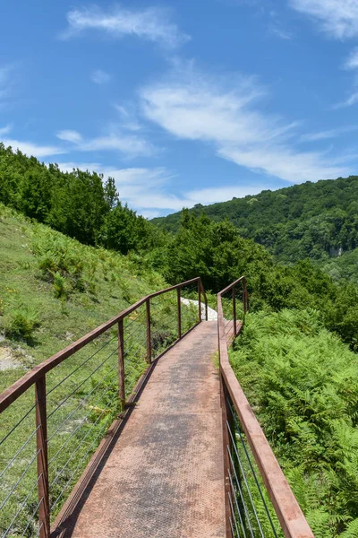 Gürcistan 'ın Gordi, Imereti bölgesindeki Okatse Kanyonu' na doğru yürüyüş yolu. Yol yeşil ağaçlarla kaplı tepelerle çevrili. Üzerinde ışık bulutları olan mavi bir gökyüzü. Gürcistan turistik merkezi
