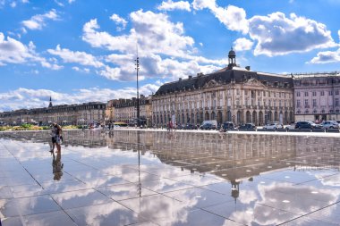 Bordeaux, Fransa - 17 Eylül 2021: Su Aynası, Place de la Bourse 'un önündeki Garonne nehrinin rıhtımındaki dünyanın en büyük yansıtma havuzu. Sokaktaki insanlar, bulutlu mavi gökyüzü