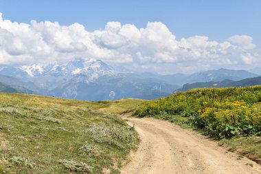 Svaneti Bölgesi, Gürcistan, Asya 'da tozlu bir yolu olan yaz dağı manzarası. Arka planda karlı dağlar var. Üzerinde bulutlar olan mavi gökyüzü. Gürcistan 'a seyahat