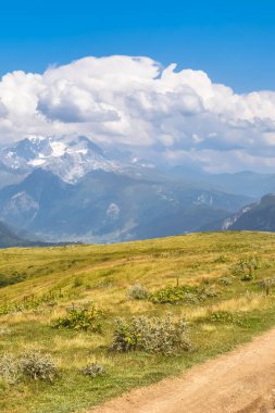 Yaz dağ manzarası, yürüyüş yolu ve arka planda karlı dağlar. Üzerinde bulutlar olan mavi gökyüzü. Gürcistan turizm beldesi