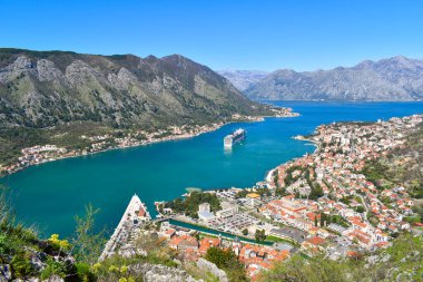Kotor, Karadağ, Avrupa. Adriyatik Denizi 'ndeki Kotor Körfezi. Eski kasabadaki binaların çatıları. Körfezde gezinti, arka planda dağlar. Açık mavi gökyüzü, güneşli gün