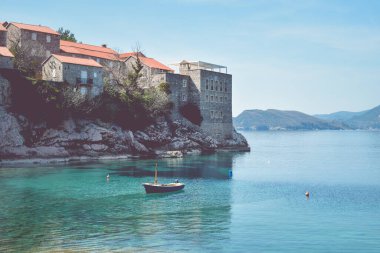 Karadağ 'ın Sveti Stefan Adası yakınlarındaki Adriyatik Denizi' nde küçük bir balıkçı teknesi. Turkuaz su, tarihi binalarla dolu bir ada. Arka planda dağlar. Balıkçılık kavramı.