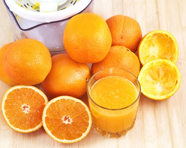 Copo de suco de laranja, casca, laranjas e espremedor . — Fotografia de Stock