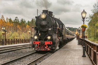 Retro buhar treni, bulutlu bir sonbahar akşamı istasyon ahşap platformundan ayrılıyor..