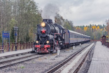Ruskeala, Rusya - 01 Ekim 2021: Retro buhar treni bulutlu bir sonbahar gününde Sortavala 'dan istasyona ahşap platforma ulaşır..