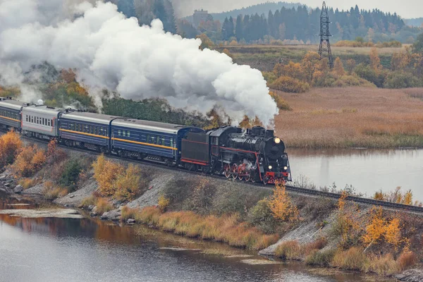 Retro trem a vapor se move ao longo do lago no outono tempo nublado. Carélia. — Fotografia de Stock