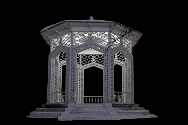 An openwork gazebo for relaxation, illuminated by evening lights in winter. Architectural landscape element isolated on black background.