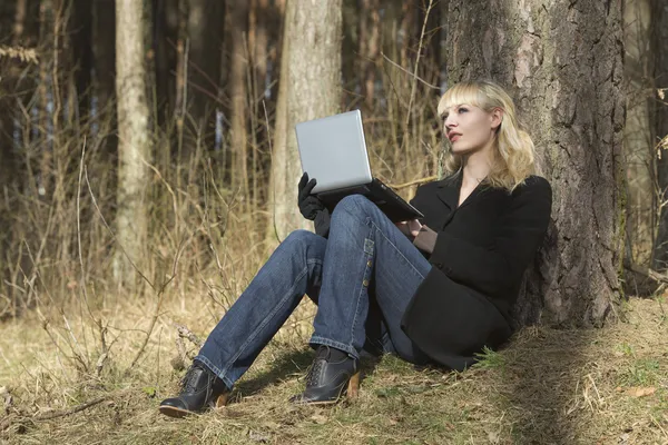 Mulher com o computador portátil senta-se em um caminho em madeira — Fotografia de Stock