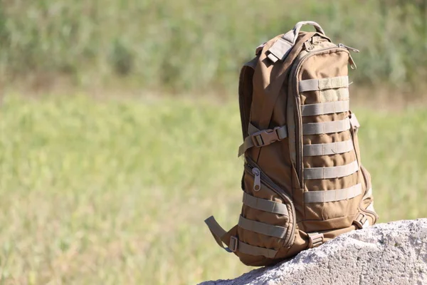 Brown military backpack close-up on the background of nature. Soldier's personal belongings.