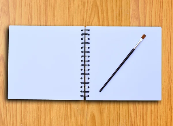 Mango de pincel en negro sobre un cuaderno de bocetos blanco y fondo de madera — Foto de Stock