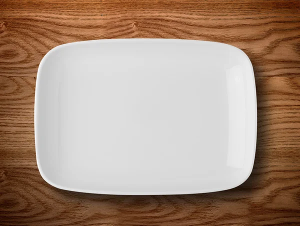 Empty white plate on wooden table — Stock Photo, Image