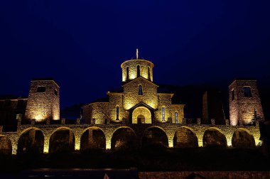 Şatoya benzeyen eski bir taş manastır. Geceleri, bina koyu mavi gökyüzüne karşı parlak sarımsı renklerle aydınlanır..