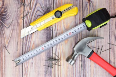 Rulet, duvar kâğıdı bıçağı, çekiç ve çiviler ahşap zemine serilmiş. Dairede küçük onarımlar için araçlar.