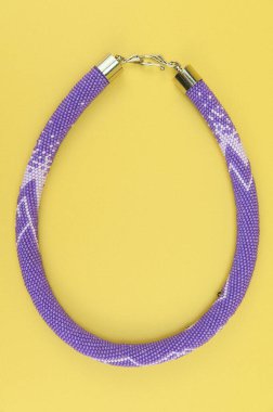 Kadın mücevherleri. Kanca kapaklı, çok renkli boncuklardan örülmüş bir kolye. Sarı arkaplanda izole edilmiş.