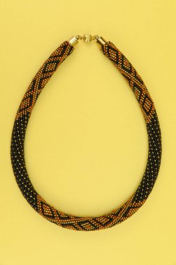 Kadın mücevherleri. Manyetik kapaklı çok renkli boncuklardan örülmüş bir kolye. Sarı arkaplanda izole edilmiş.