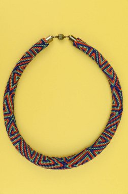 Kadın mücevherleri. Manyetik kapaklı çok renkli boncuklardan örülmüş bir kolye. Sarı arkaplanda izole edilmiş.