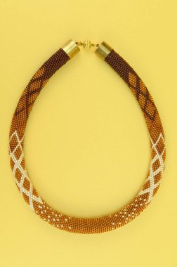 Kadın mücevherleri. Manyetik kapaklı çok renkli boncuklardan örülmüş bir kolye. Sarı arkaplanda izole edilmiş.