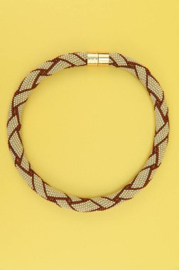 Kadın mücevherleri. Manyetik kapaklı çok renkli boncuklardan örülmüş bir kolye. Sarı arkaplanda izole edilmiş.