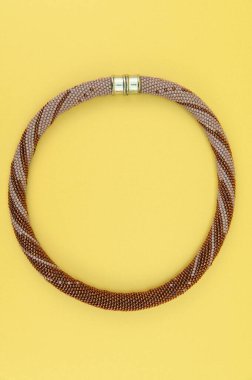 Kadın mücevherleri. Manyetik kapaklı çok renkli boncuklardan örülmüş bir kolye. Sarı arkaplanda izole edilmiş.