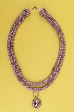 Kadın mücevherleri. Manyetik kapaklı çok renkli boncuklardan örülmüş bir kolye. Sarı arkaplanda izole edilmiş.